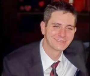 Brad dressed in a sharp suit, smiling confidently after attending his mom's wedding.